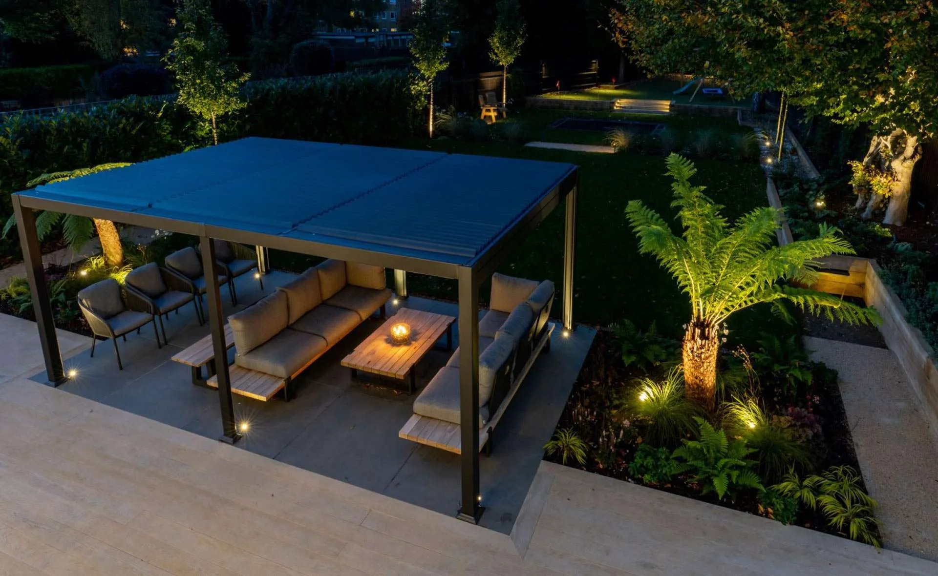 Night time garden with porcelain patio and steel pergola and lush tropical planting