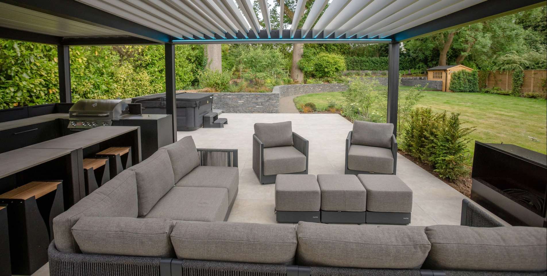 Contemporary Social Family Garden in Harpenden, Hertfordshire featuring porcelain paving, slate clad walls, hot tub and steel pergola with outdoor dining and lounge seating areas and large family garden