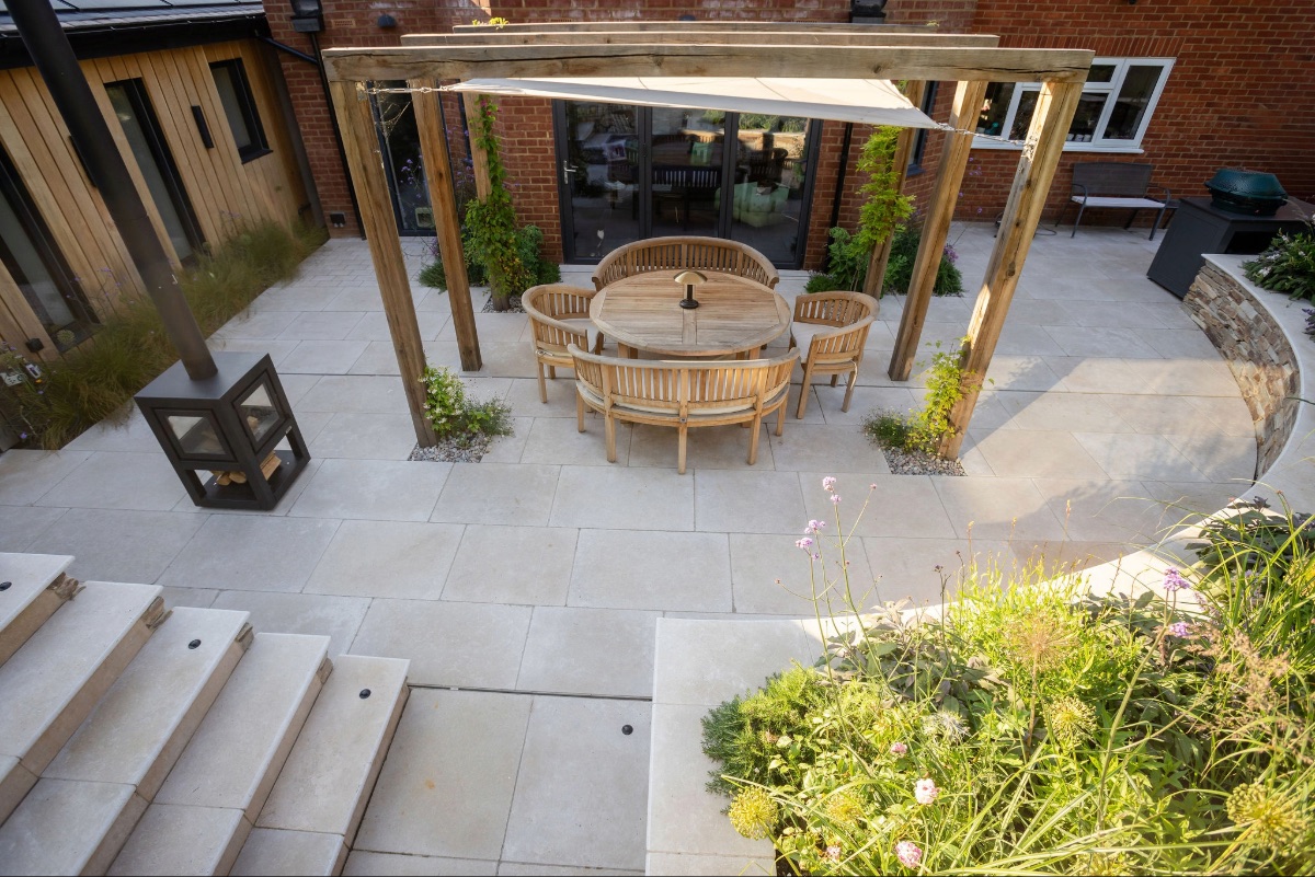 Pale beige limestone steps with oak arches, outdoor dining table and chairs and curved raised planted bed