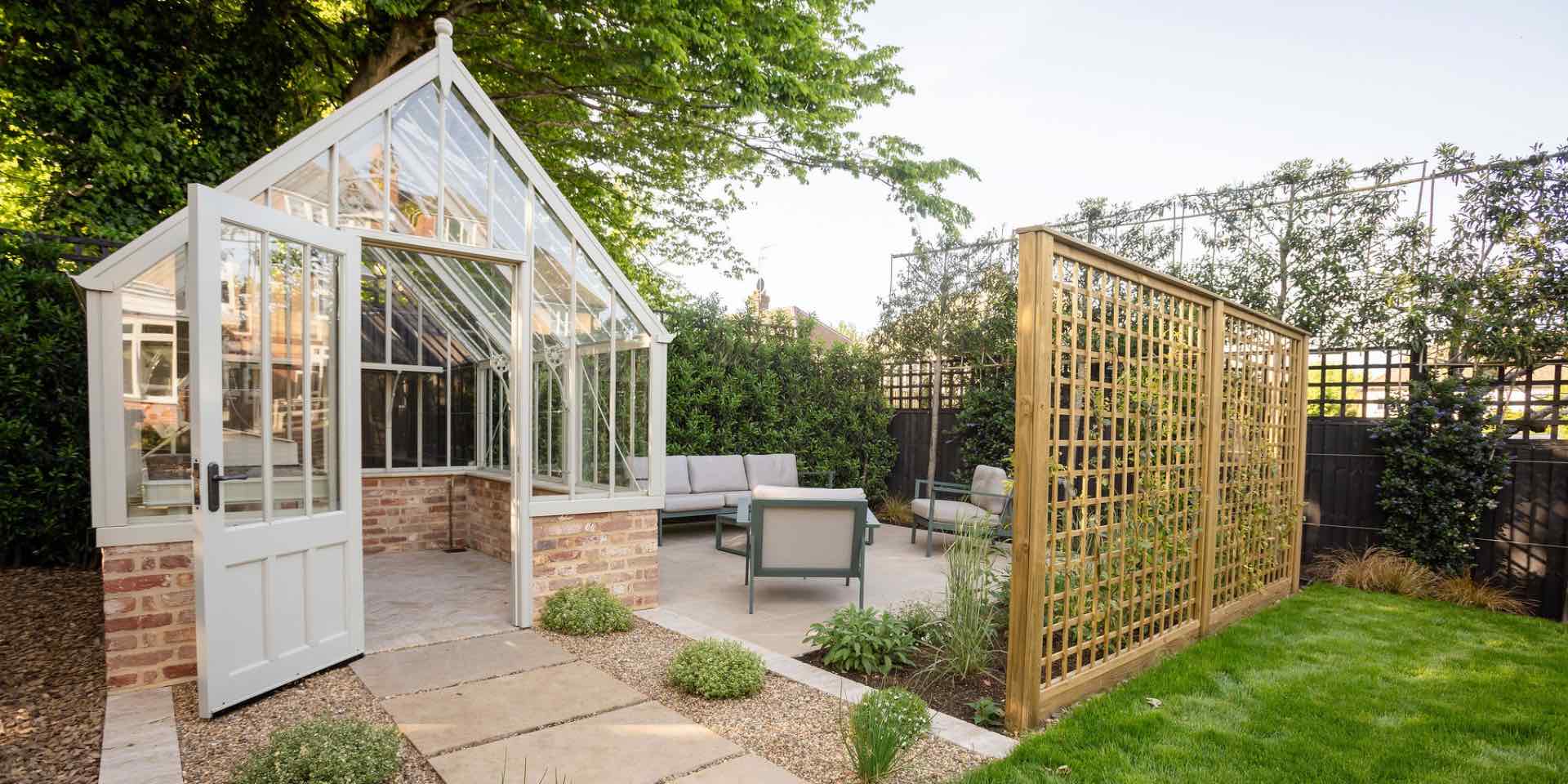 Pale green Alitex aluminium greenhouse with limestone stepping stones in pebbles with plants and limestone paved outdoor lounge area