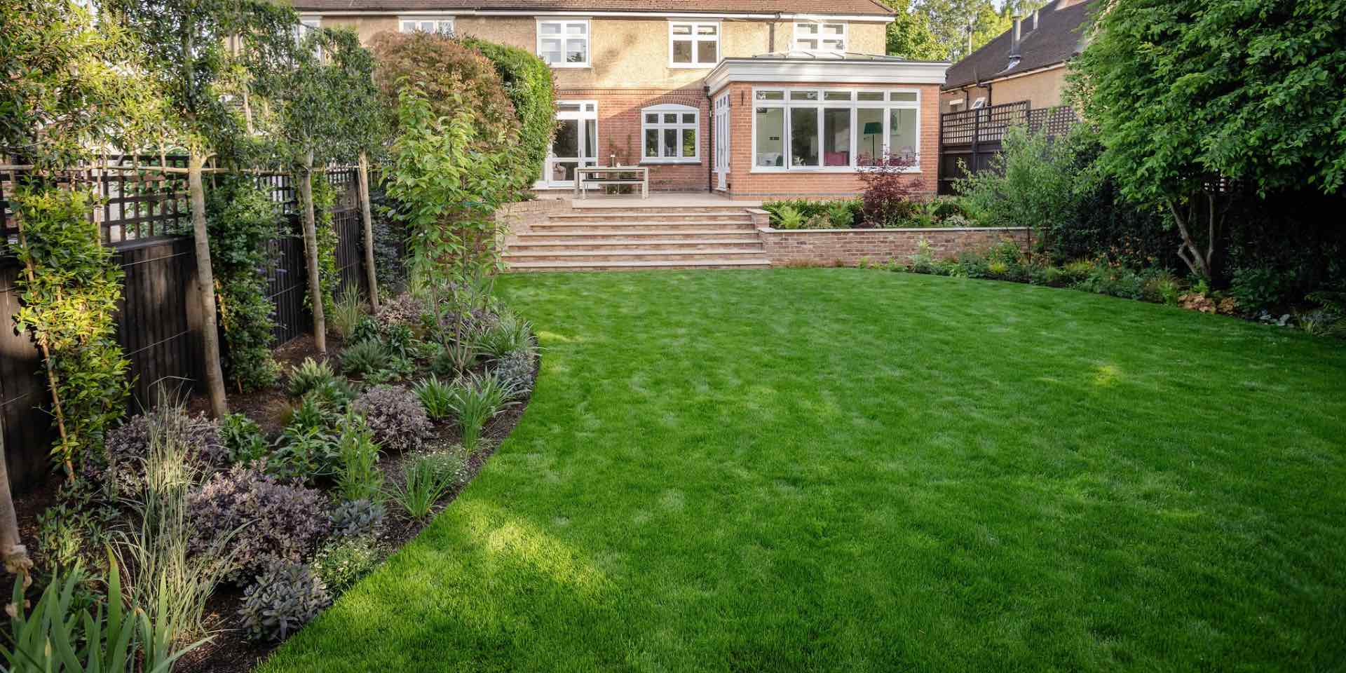 Curved lawn with planted borders for sun and wide limestone steps and planter