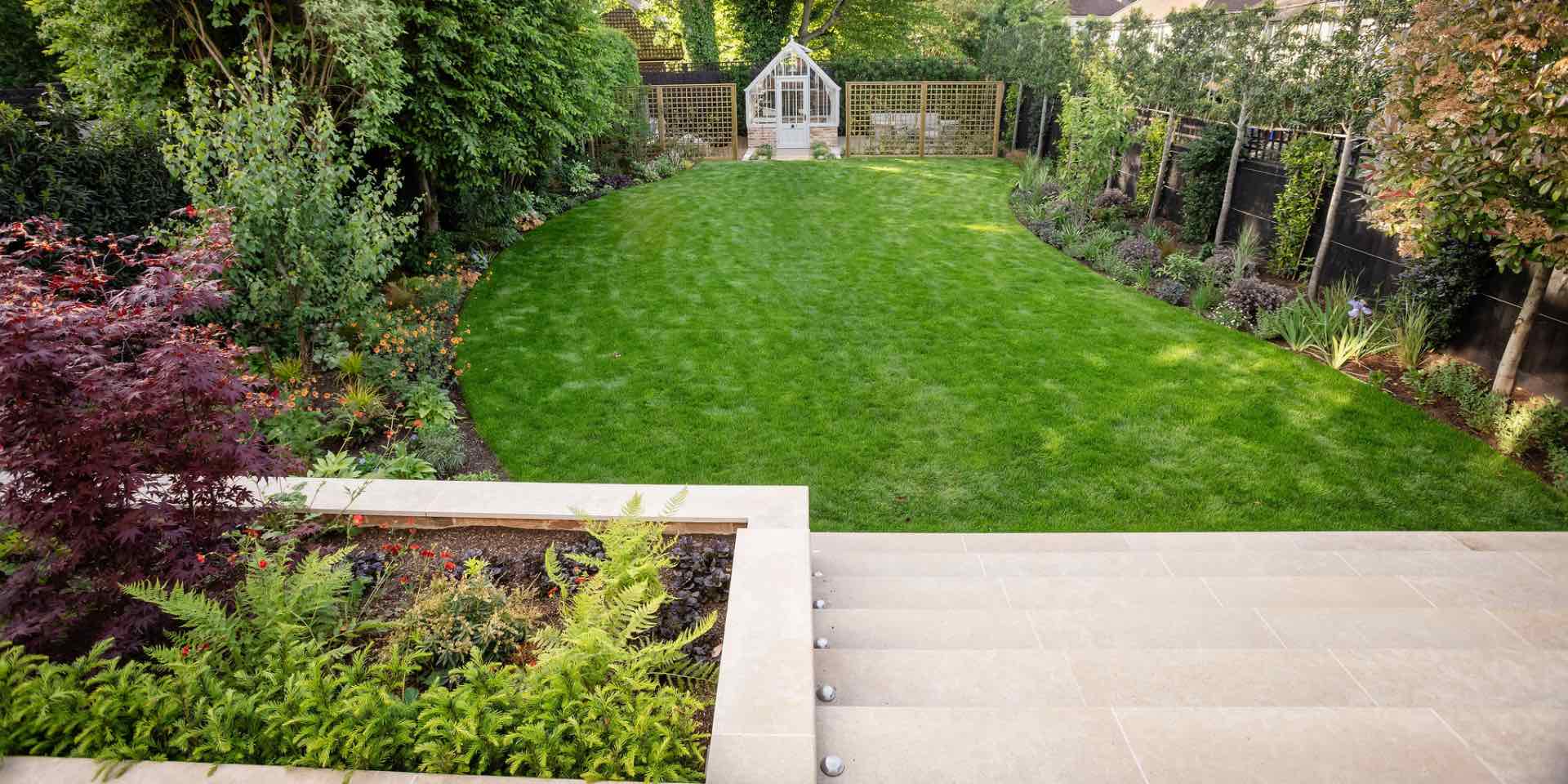 Small town garden with sweeping curved lawn, limestone paving and planting and Alitex greenhouse with trellis