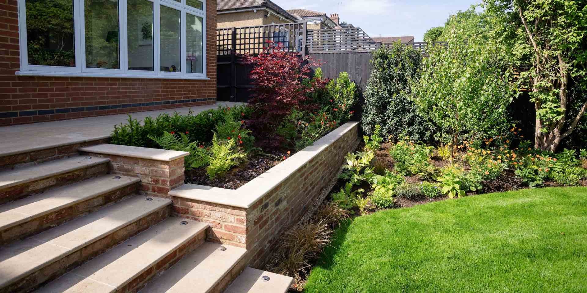 Limestone paved steps and terraced planters with limestone copings with mixed planting for shade including Acer palmatum Bloodgood'