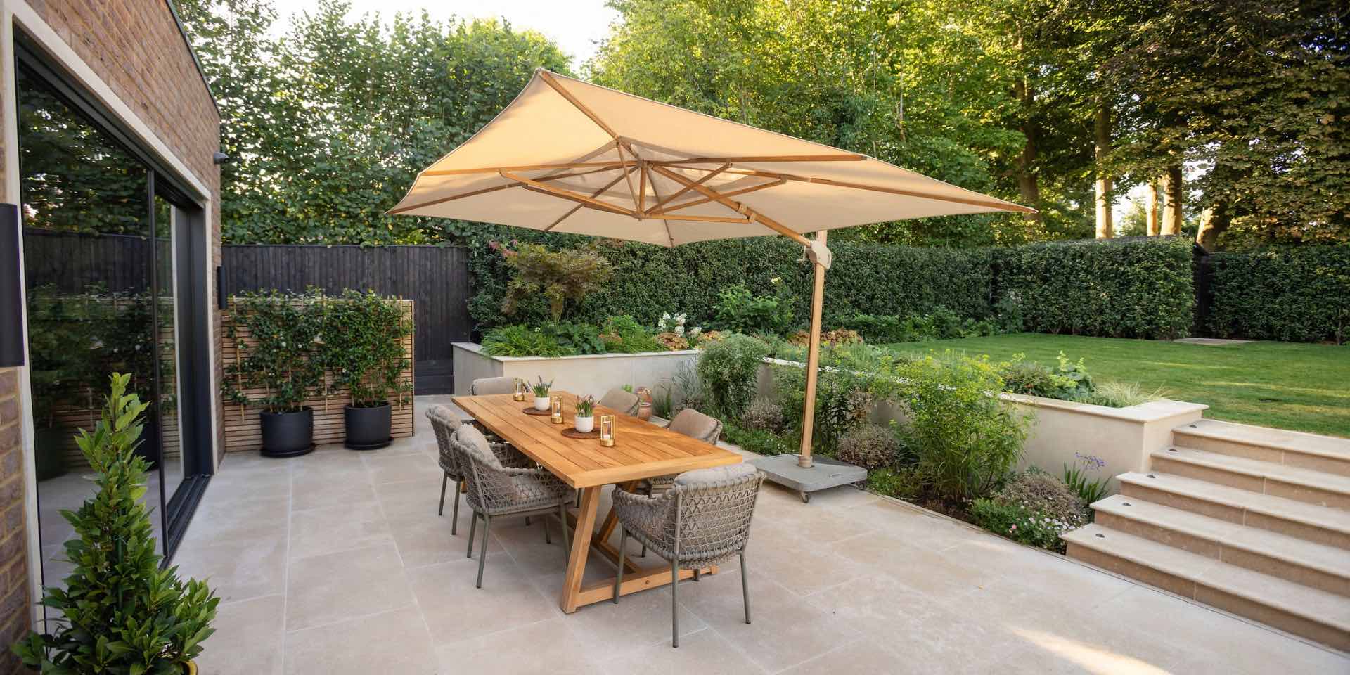 Large teak dining table and chairs in beautiful luxury Harpenden garden with limestone paving, porcelain clad walls, colourful naturalistic planting and cantilever parasol