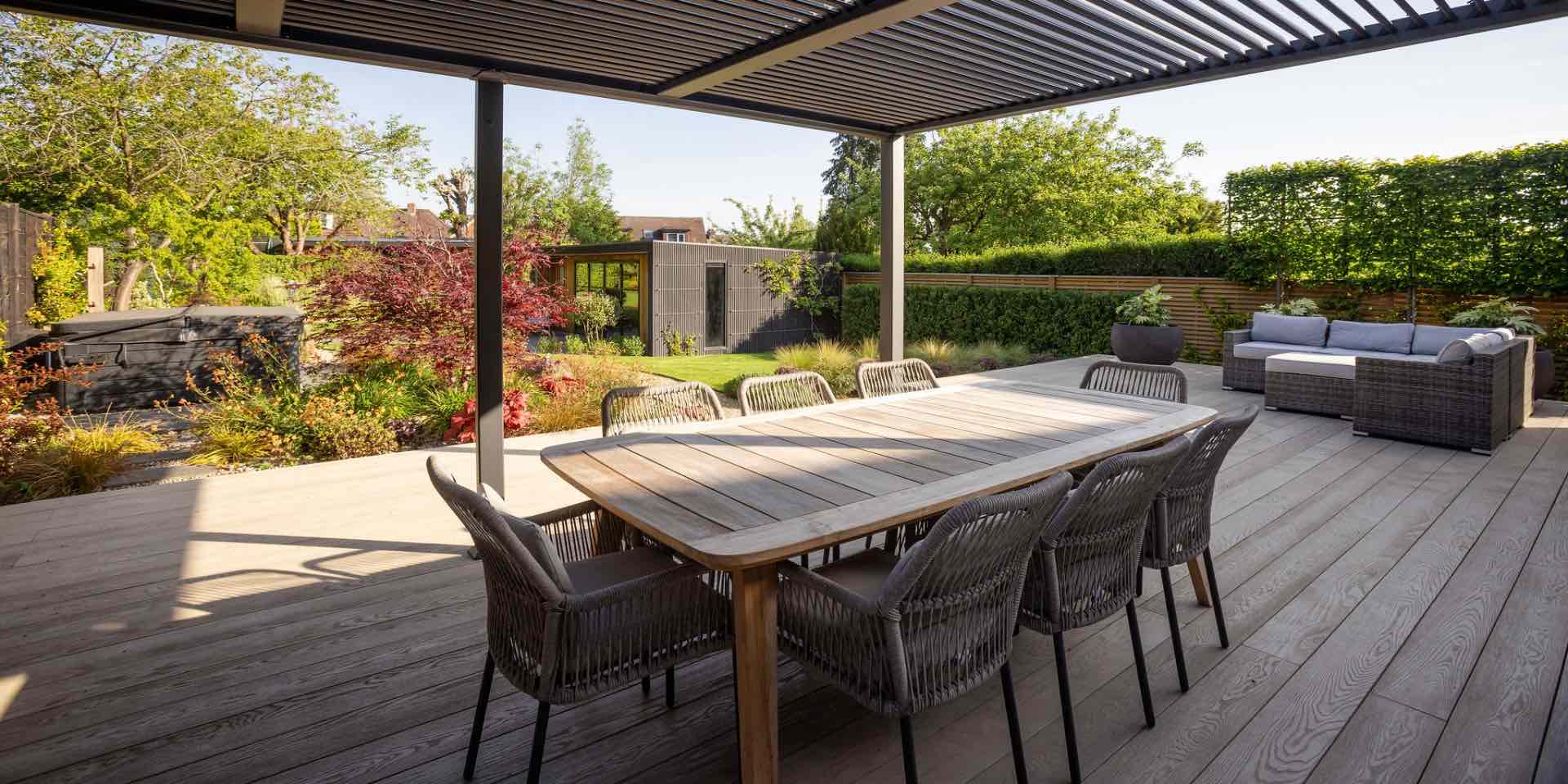 Garden Design for large decked outdoor lounge and dining area with steel pergola and garden room in the background in Harpenden
