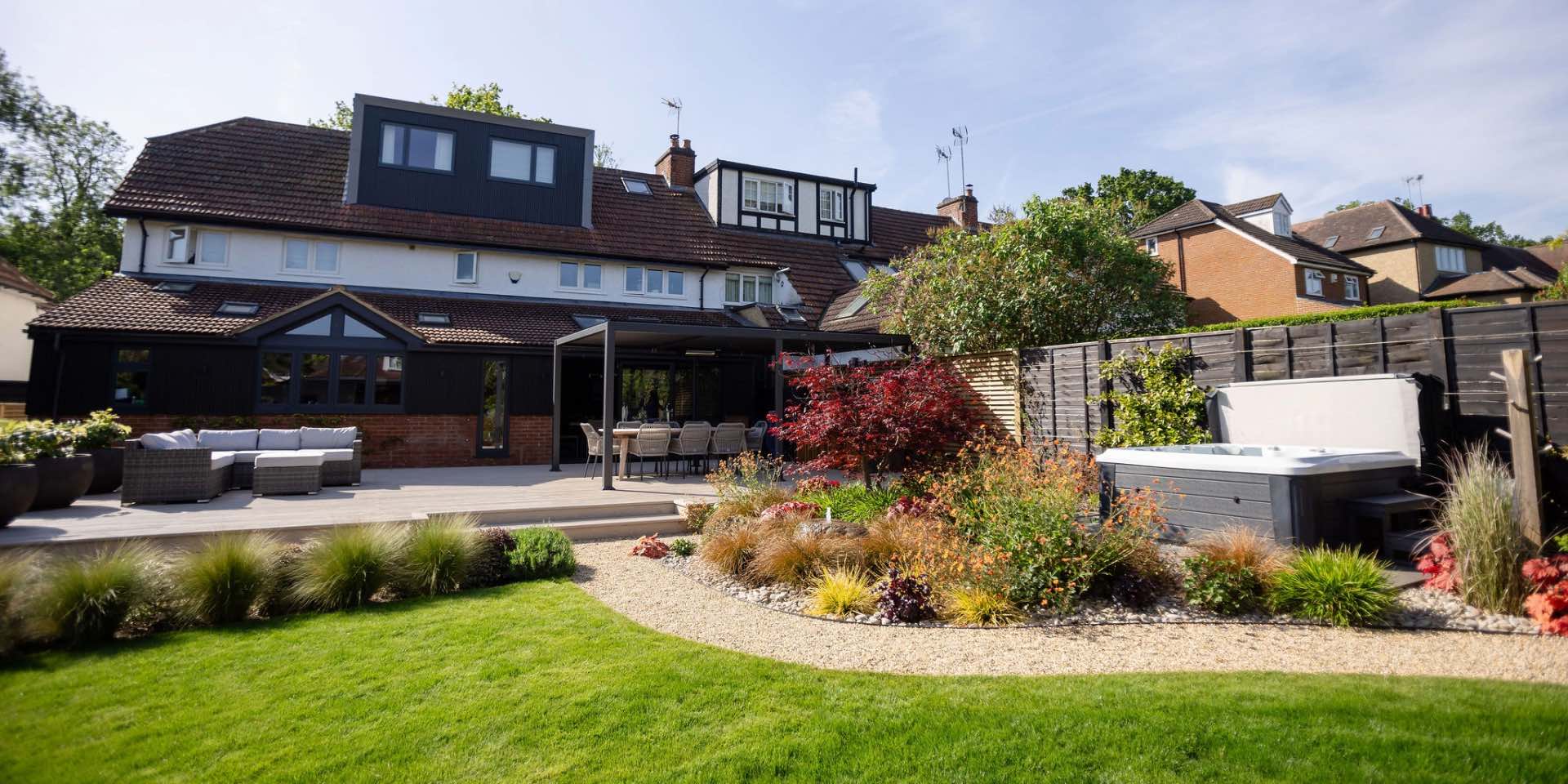 Large family garden in Harpenden with curving path wrapping around pebble planted border with stepping stones to Hot Tub. Large composite deck with steel pergola and outdoor dining table and lounge seating