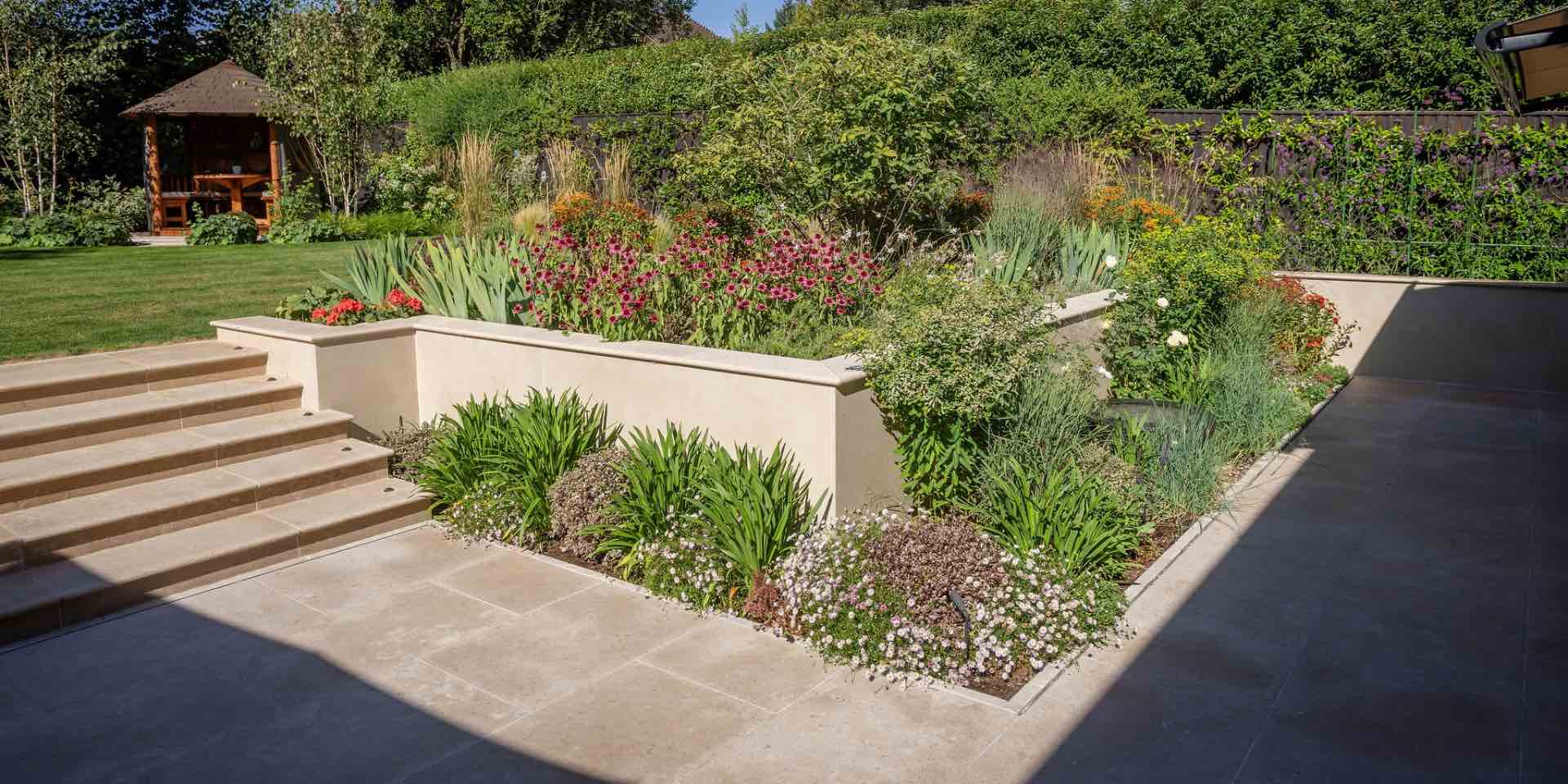 Limestone steps and paving with a sunken seating area and porcelain clad retaining walls with extensive colourful perennial and evergreen planting for sun
