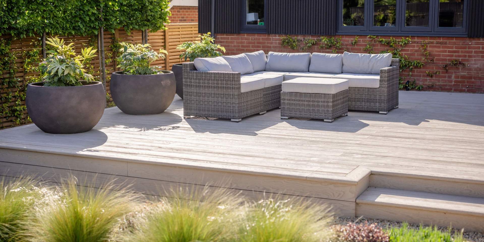 Millboard Composite Deck in Limed Oak with grey outdoor corner sofa and large circular planters with Fats japonica