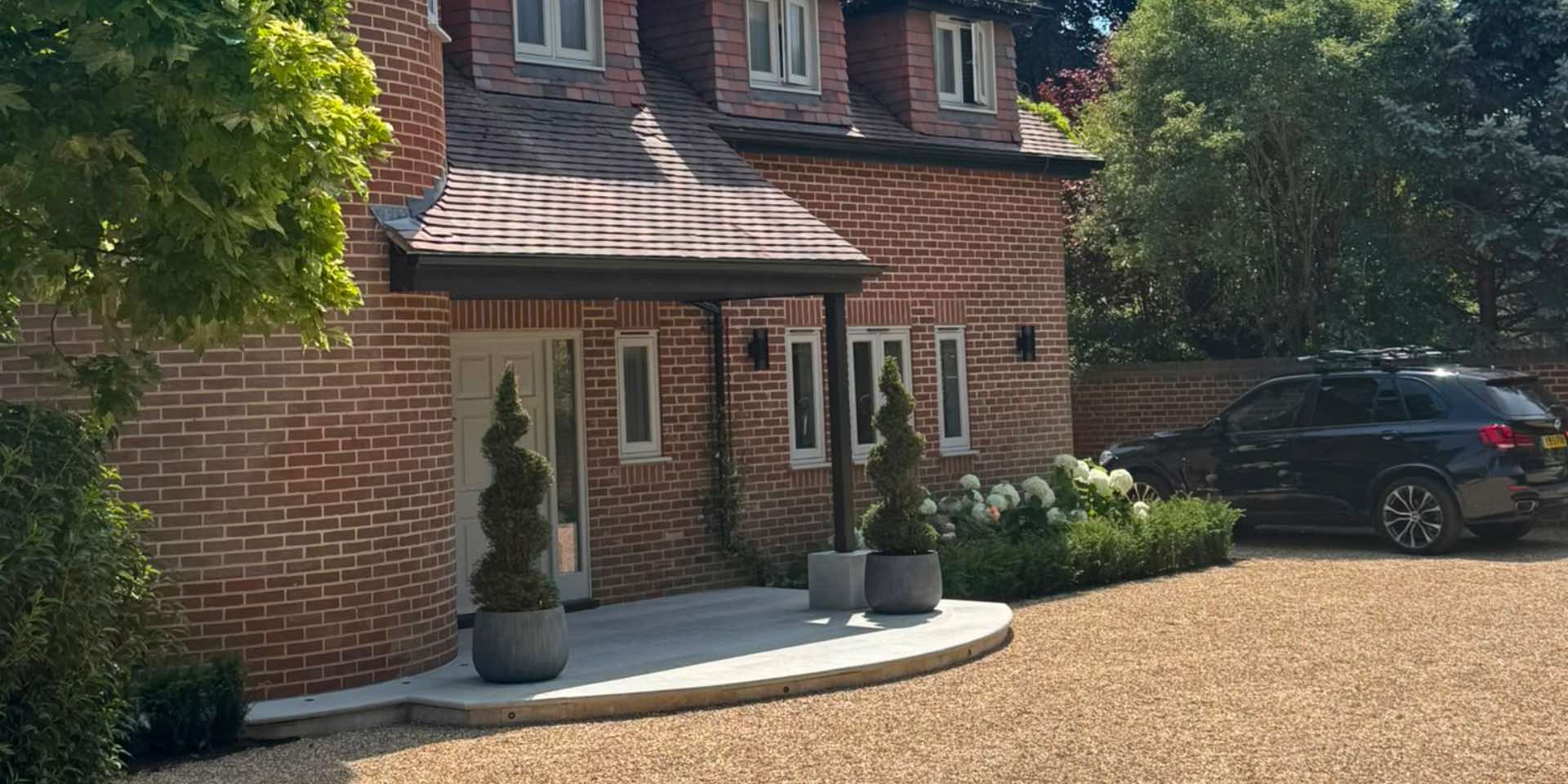 Jura Grey Limestone Paving from London Stone to create a curving entrance platform to a front door. Two circular planters with Taxus spirals.
