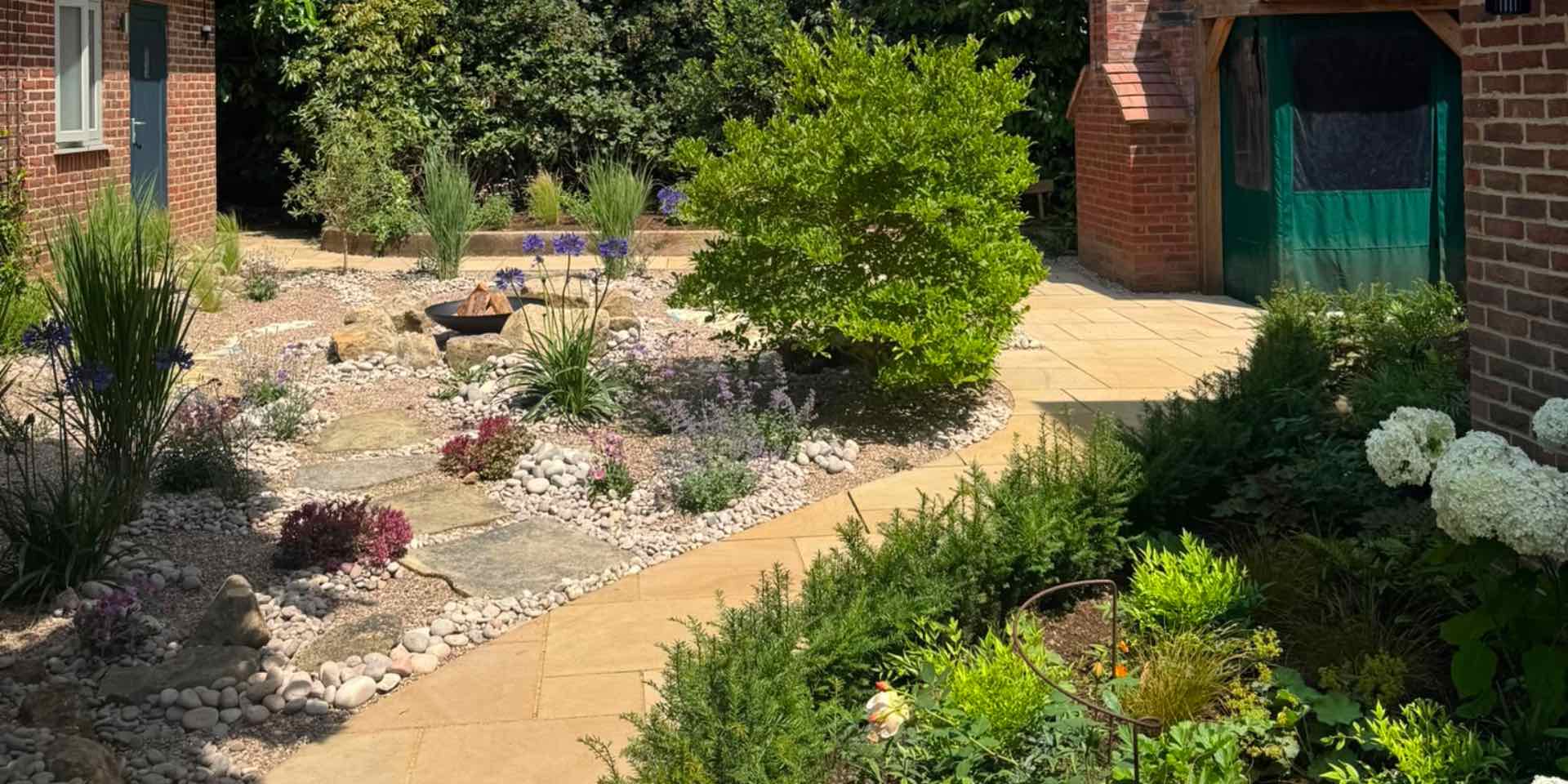 Stepping stones in pebble planting area to timber curved firepit seating with mediterranean planting