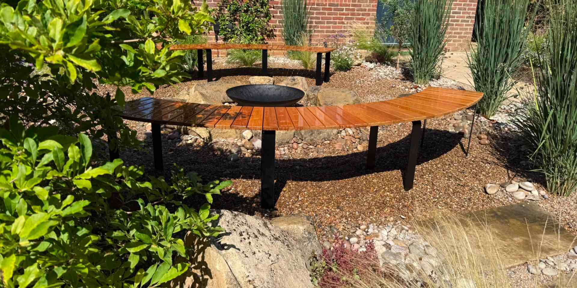 Timber slatted seating in curve around a circular cast iron fire bowl with pebbles