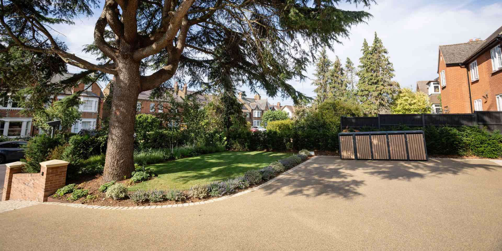 Large resin bound drive in front garden in Hertford with bin storage, large lawn and mixed planting with granite sett edging