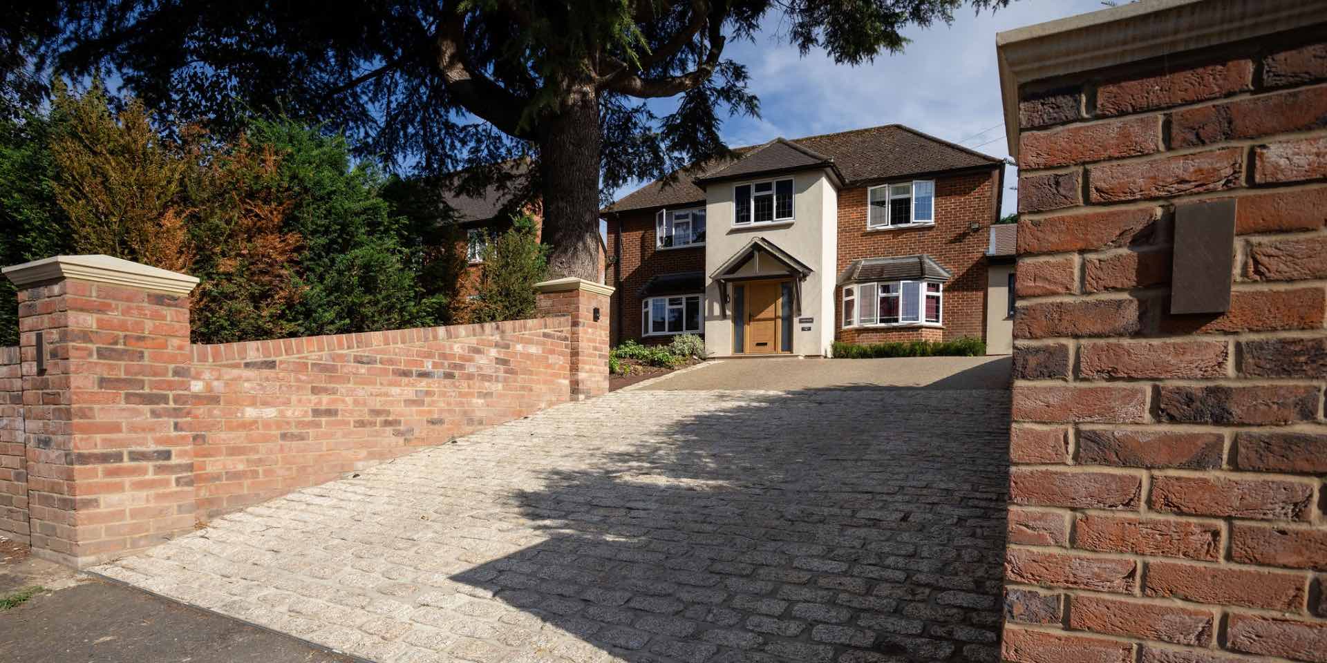 Tumbled yellow granite setts which form a driveway crossover onto a resin bound gravel drive with red brick retaining walls and natural stone pier caps