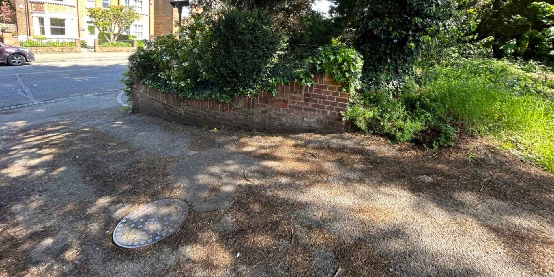 Hertford driveway and boundary wall before re-design, with large manhole cover, tarmac drive and overgrown garden
